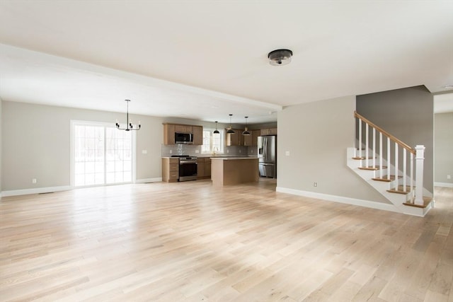 unfurnished living room with baseboards, light wood-style flooring, an inviting chandelier, and stairs