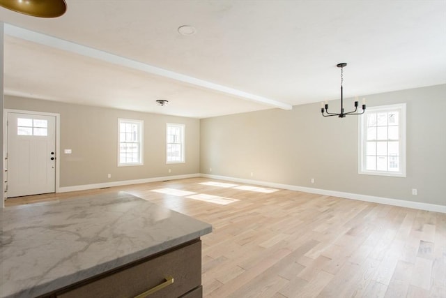 unfurnished living room with light wood-type flooring, beam ceiling, baseboards, and an inviting chandelier