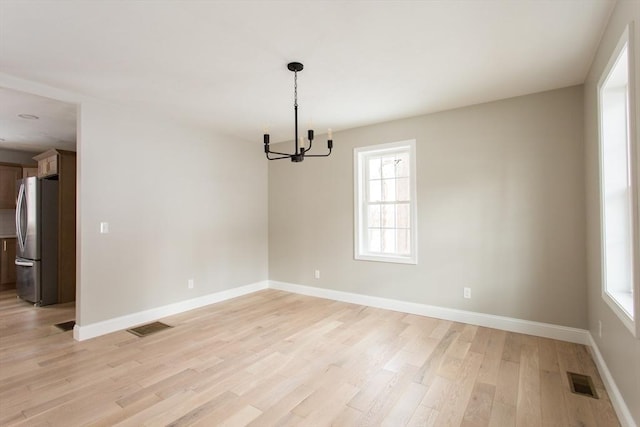 empty room with light wood-style floors, visible vents, plenty of natural light, and baseboards