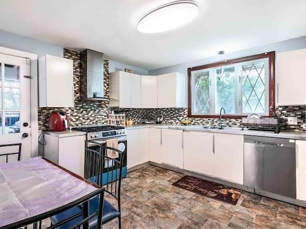 26 Beulah St, Framingham, MA 01701 - kitchen featuring appliances with stainless steel finishes, wall chimney range hood, light countertops, backsplash, and stone finish flooring