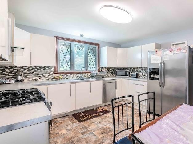 26 Beulah St, Framingham, MA 01701 - kitchen with stainless steel appliances, white cabinets, light countertops, decorative backsplash, and stone finish floors