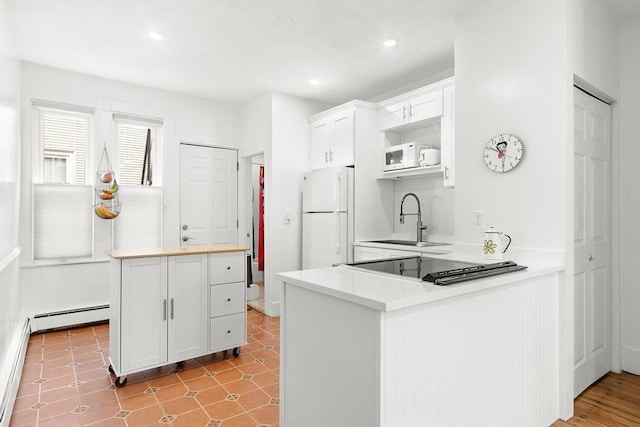 kitchen with baseboard heating, a sink, light countertops, white appliances, and white cabinetry