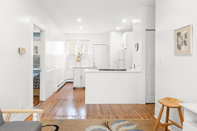 kitchen with white cabinets, baseboard heating, light wood-style floors, freestanding refrigerator, and a peninsula