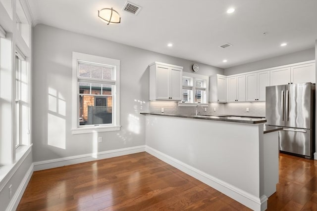 kitchen featuring kitchen peninsula, stainless steel fridge, dark hardwood / wood-style flooring, white cabinets, and tasteful backsplash