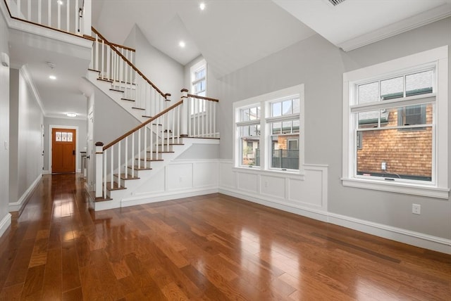 unfurnished living room featuring a towering ceiling, crown molding, hardwood / wood-style floors, and a wealth of natural light