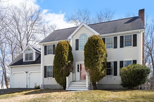 colonial inspired home with driveway, roof with shingles, a chimney, a front lawn, and a garage