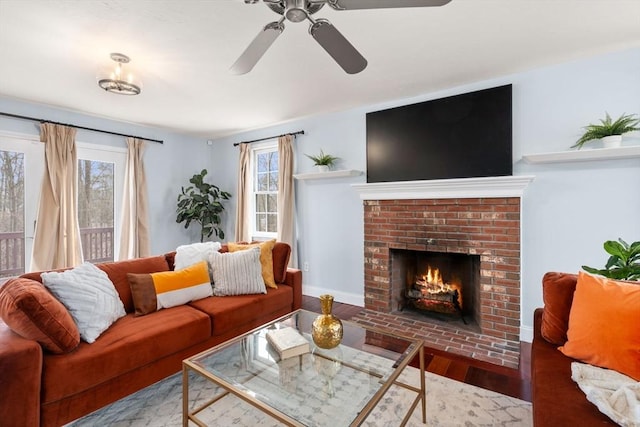 living room featuring ceiling fan, baseboards, a brick fireplace, and wood finished floors