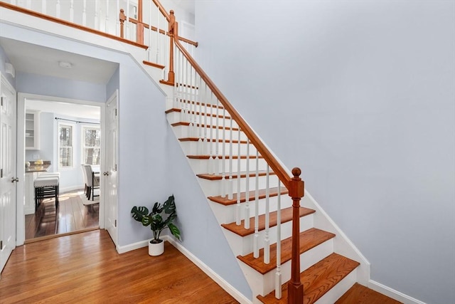 stairs featuring a high ceiling, baseboards, and wood finished floors