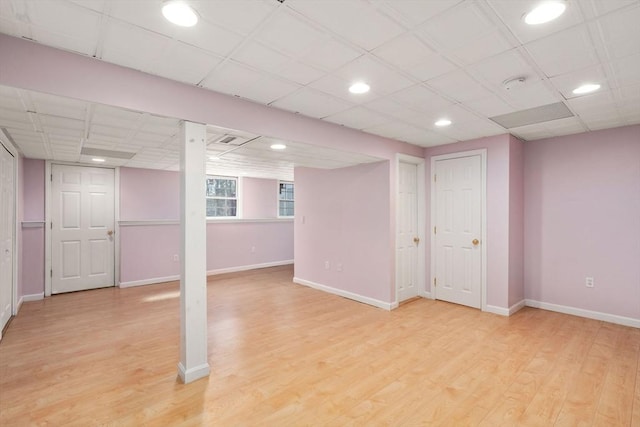 below grade area featuring baseboards, light wood-type flooring, and a paneled ceiling