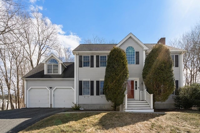 colonial-style house featuring roof with shingles, a garage, driveway, and a chimney