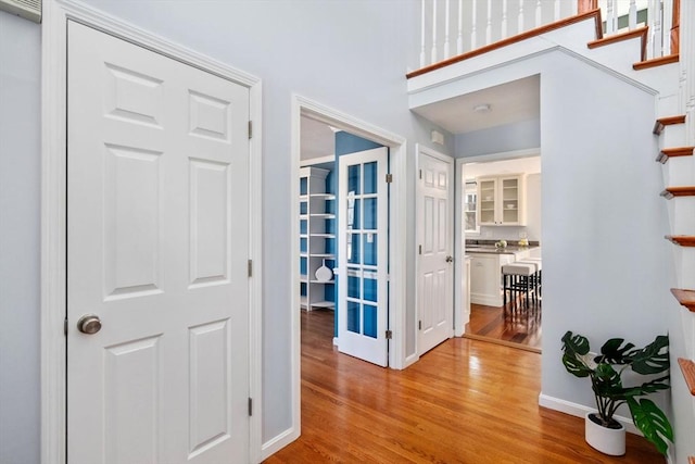 hall with light wood-type flooring, baseboards, and stairs