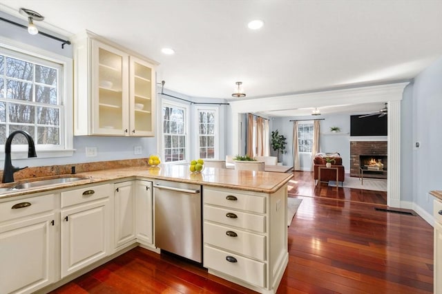 kitchen featuring a peninsula, a fireplace, dark wood-style flooring, a sink, and stainless steel dishwasher