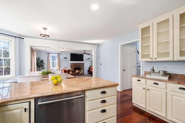 kitchen featuring light stone counters, dark wood-type flooring, glass insert cabinets, dishwasher, and a brick fireplace