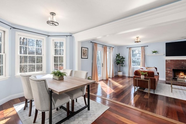 dining space featuring baseboards, wood-type flooring, and a brick fireplace