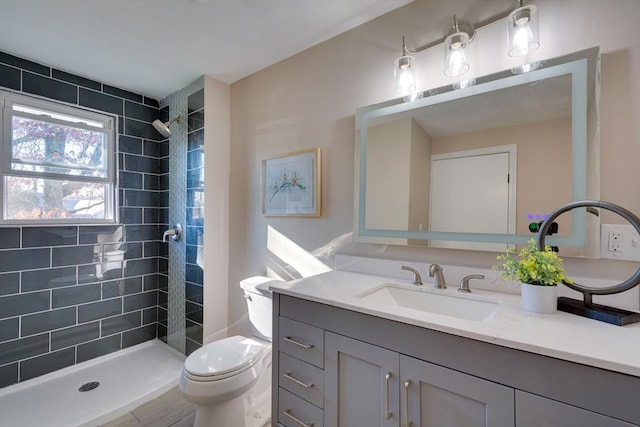 bathroom featuring a tile shower, vanity, and toilet