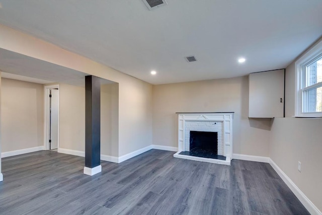 unfurnished living room with a brick fireplace and dark wood-type flooring