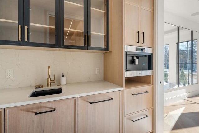 kitchen with glass insert cabinets, oven, light brown cabinets, and a sink