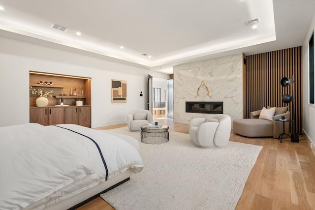 bedroom with light wood-style floors, visible vents, a tray ceiling, and a high end fireplace