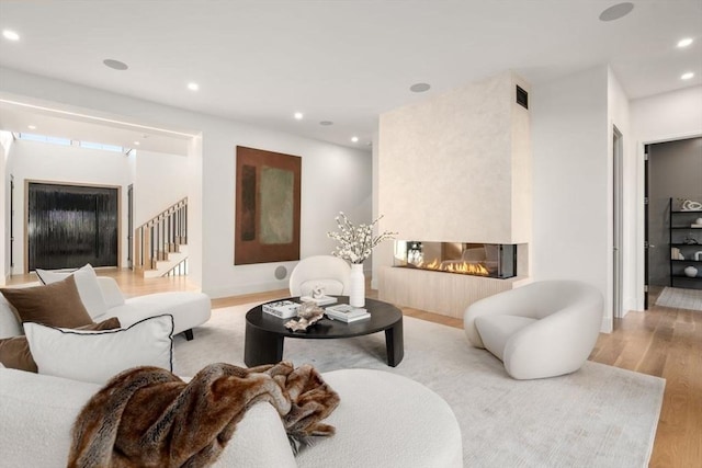 living area with recessed lighting, visible vents, light wood-style floors, stairway, and a glass covered fireplace