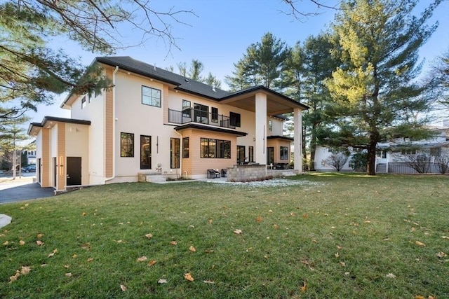 back of house featuring a lawn, a patio, a balcony, fence, and stucco siding