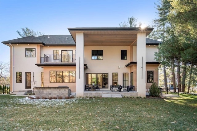 back of house featuring a balcony, stucco siding, a lawn, and a patio