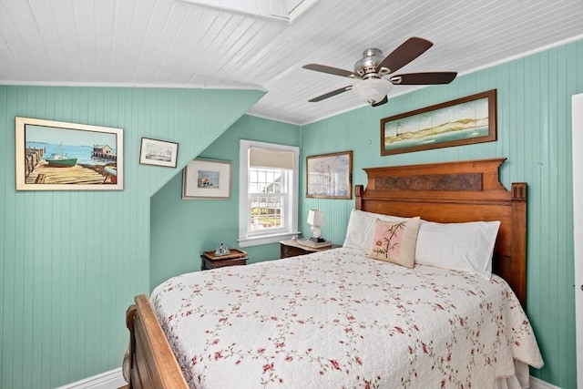 bedroom with ceiling fan, wooden walls, and ornamental molding