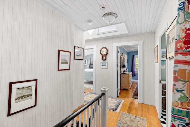 hall featuring light wood-type flooring, a skylight, wood walls, and wooden ceiling