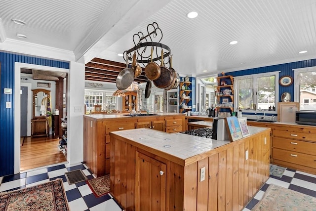 kitchen with kitchen peninsula, tile counters, stainless steel gas cooktop, ornamental molding, and sink