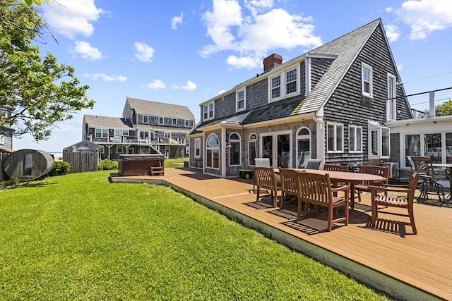 rear view of house featuring a wooden deck, a hot tub, and a lawn