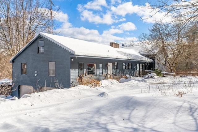 snow covered house featuring a chimney and an attached garage