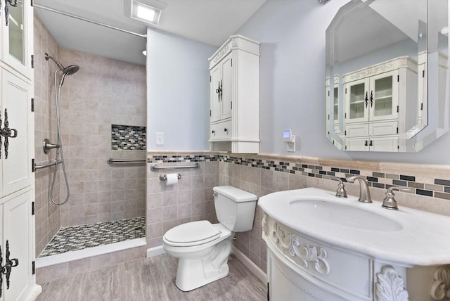 bathroom with tiled shower, vanity, toilet, and tile walls