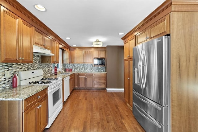 kitchen featuring white appliances, sink, tasteful backsplash, light hardwood / wood-style floors, and light stone counters