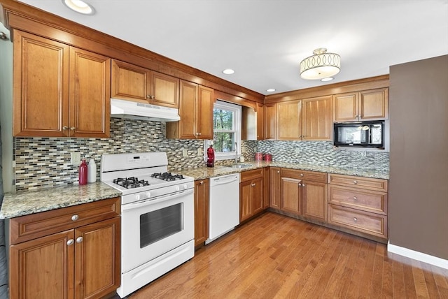 kitchen with light stone countertops, sink, light hardwood / wood-style flooring, backsplash, and white appliances