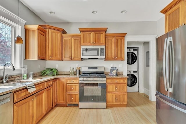 kitchen featuring stainless steel appliances, stacked washer / drying machine, a sink, and light wood finished floors