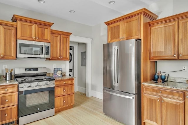 kitchen featuring brown cabinetry, appliances with stainless steel finishes, light stone countertops, light wood-style floors, and recessed lighting