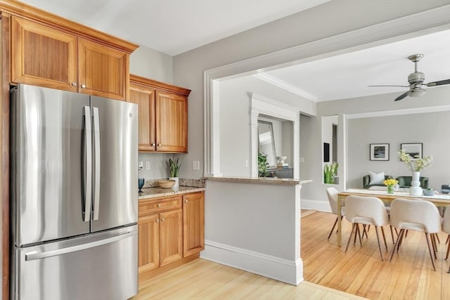 kitchen featuring ceiling fan, light stone countertops, light wood-style floors, freestanding refrigerator, and baseboards