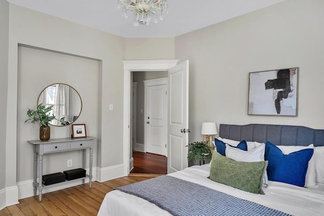 bedroom with an inviting chandelier, baseboards, and wood finished floors