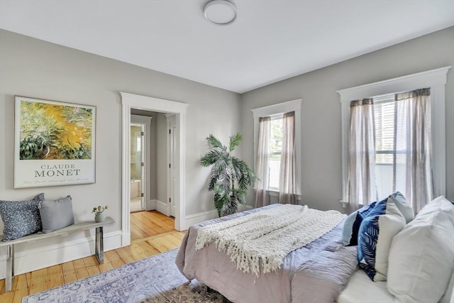 bedroom with connected bathroom, baseboards, and wood finished floors