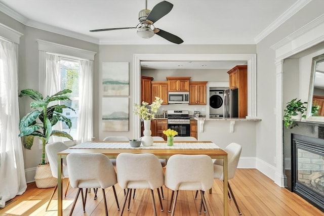 dining space featuring light wood-style floors, a ceiling fan, stacked washer and dryer, and a glass covered fireplace