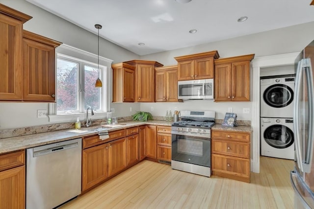 kitchen featuring light wood-style floors, appliances with stainless steel finishes, light stone counters, and stacked washing maching and dryer