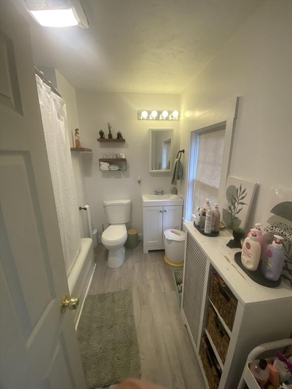 full bathroom featuring shower / bathtub combination with curtain, toilet, vanity, and hardwood / wood-style flooring