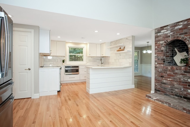 kitchen with white cabinets, light hardwood / wood-style floors, decorative light fixtures, and appliances with stainless steel finishes