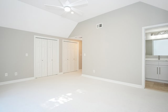 unfurnished bedroom with two closets, light colored carpet, vaulted ceiling, ceiling fan, and connected bathroom