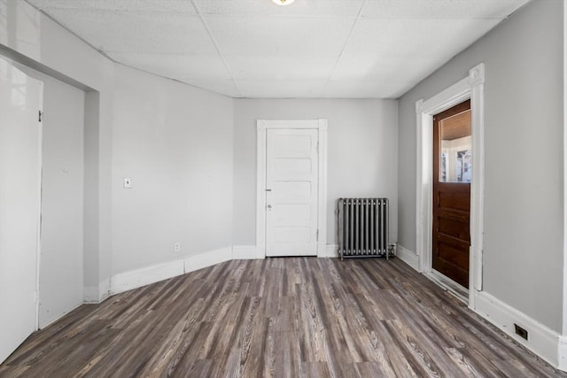 unfurnished room featuring a drop ceiling, radiator, and dark hardwood / wood-style floors