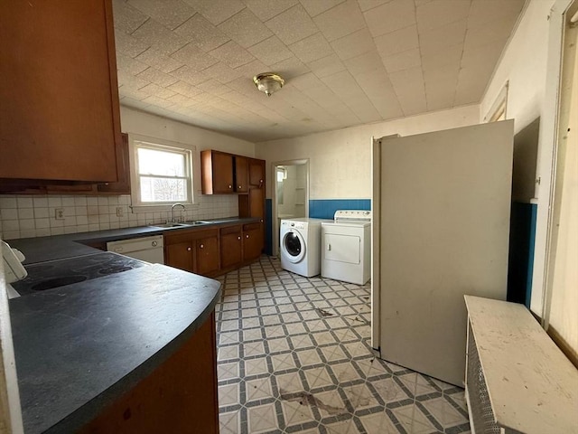 kitchen featuring washer and dryer, a sink, backsplash, dark countertops, and light floors