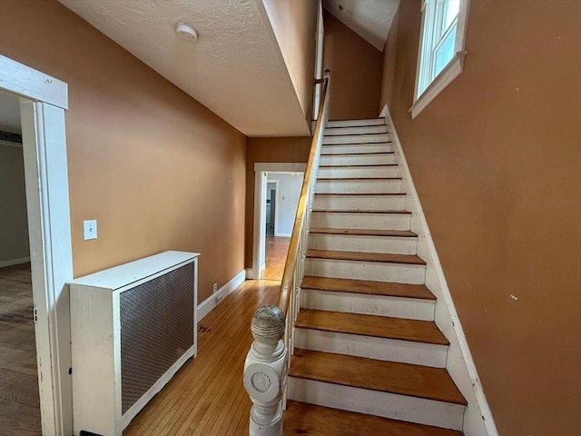 staircase with heating unit, a textured ceiling, baseboards, and wood finished floors