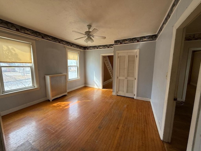 unfurnished bedroom with ceiling fan, baseboards, radiator heating unit, hardwood / wood-style floors, and a textured ceiling