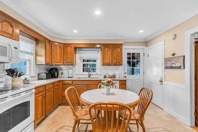 kitchen with sink, backsplash, light stone counters, crown molding, and white appliances