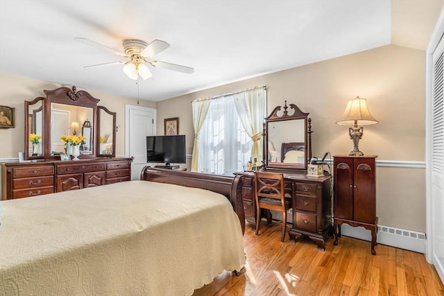 bedroom with lofted ceiling, a baseboard heating unit, ceiling fan, light hardwood / wood-style floors, and a closet