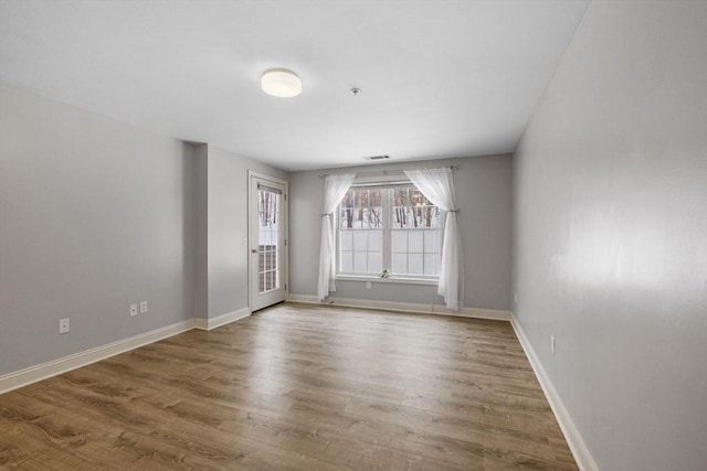 unfurnished room with wood finished floors, visible vents, and baseboards